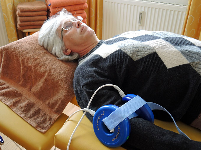 Foto
                        vom Arthrotun-Gert von Dr. Mamat in Anwendung
                        mit Vitalisierungseinheiten am Oberarm eines
                        Patienten angebracht